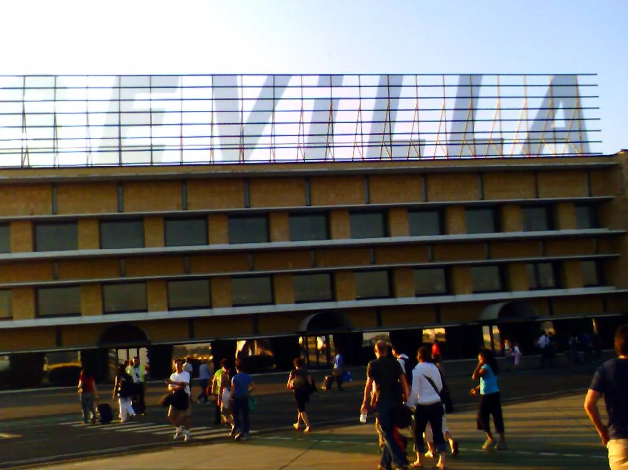 Historic exterior view of Seville Airport terminal with travellers outside