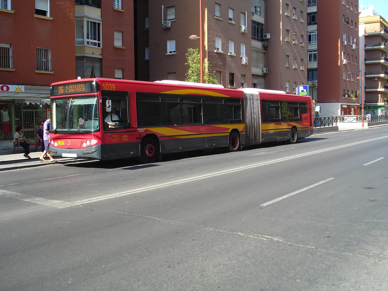 Red articulated TUSSAM city bus displaying route 06 on a Seville street
